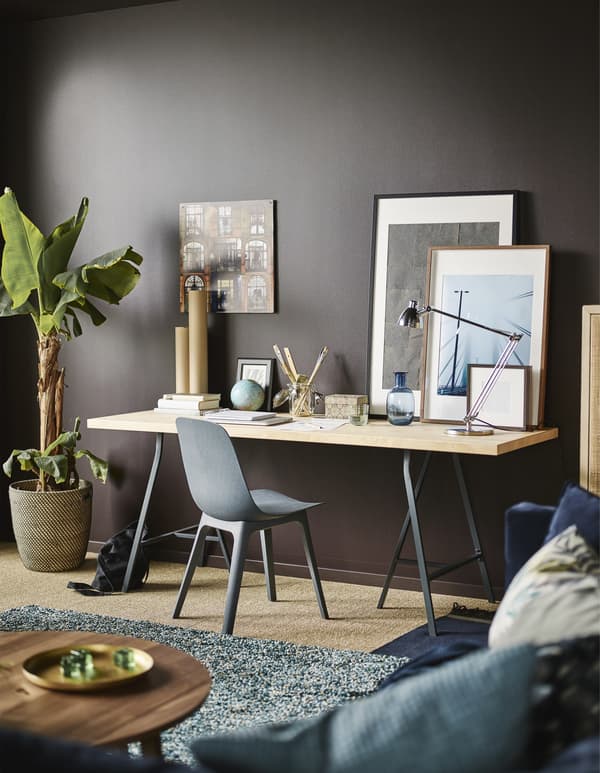 Estación de trabajo compuesta de una silla y un gran escritorio contra la pared marrón oscuro de un salón moderno.