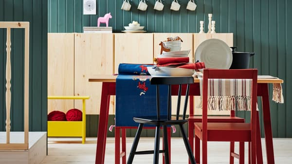 Estancia con mesa, silla, taburete, armario de madera, camino de mesa azul, vajilla blanca, candelabro y pared de madera verde.
