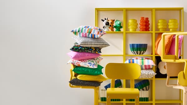Estante amarillo junto a silla amarilla con cojines de muchos colores.