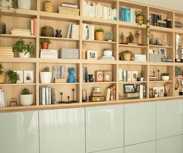 Estantería de madera que cubre toda una pared dividida en dos, la parte de arriba con estantes llenos de libros y adornos y la parte de abajo con puertas que cubren el contenido.