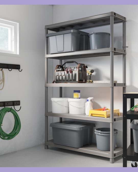 Estantería de plástico gris en un garaje o bodega, con cajas grandes, baldes, herramientas y productos de limpieza organizados en cuatro niveles.