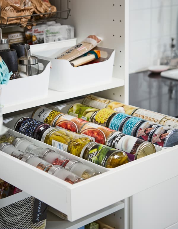 Estantes e un caixón aberto nun armario de cociña con latas, especias e tarros perfectamente organizados.