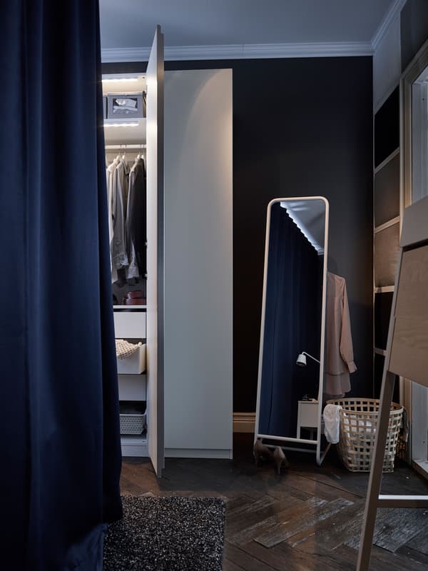 Este armario de dormitorio branco con luces incorporadas está xunto a un espello con almacenaxe para roupa.