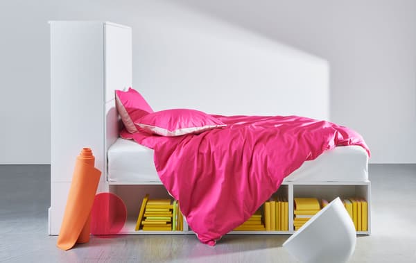 Estrutura de cama em branco com arrumação integrada e com roupa de cama cor de rosa.