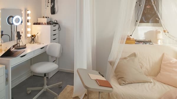 Et ALEX skrivebord og et ALEX skuffeelement danner et område til påklædning. En BJÖRKÅSEN støtte til bærbar computer og en LYCKSELE HÅVET sovesofa står i nærheden.