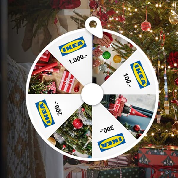 Et hjul, der spinner og hvor hver anden ege viser et IKEA logo i baggrunden ses en person, der er ved at pynte et juletræ.