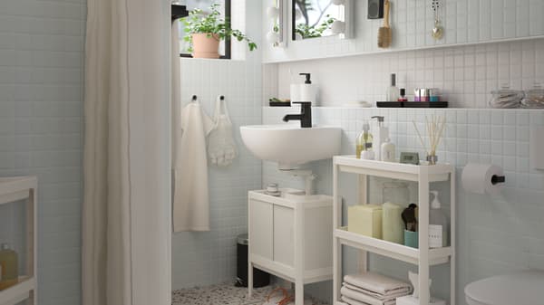 Et hvidt LILLTJÄRN/SKATSJÖN badeværelsesmøbel med en SALJEN vandhane ved siden af et hvidt VESKEN rullebord med toiletartikler.