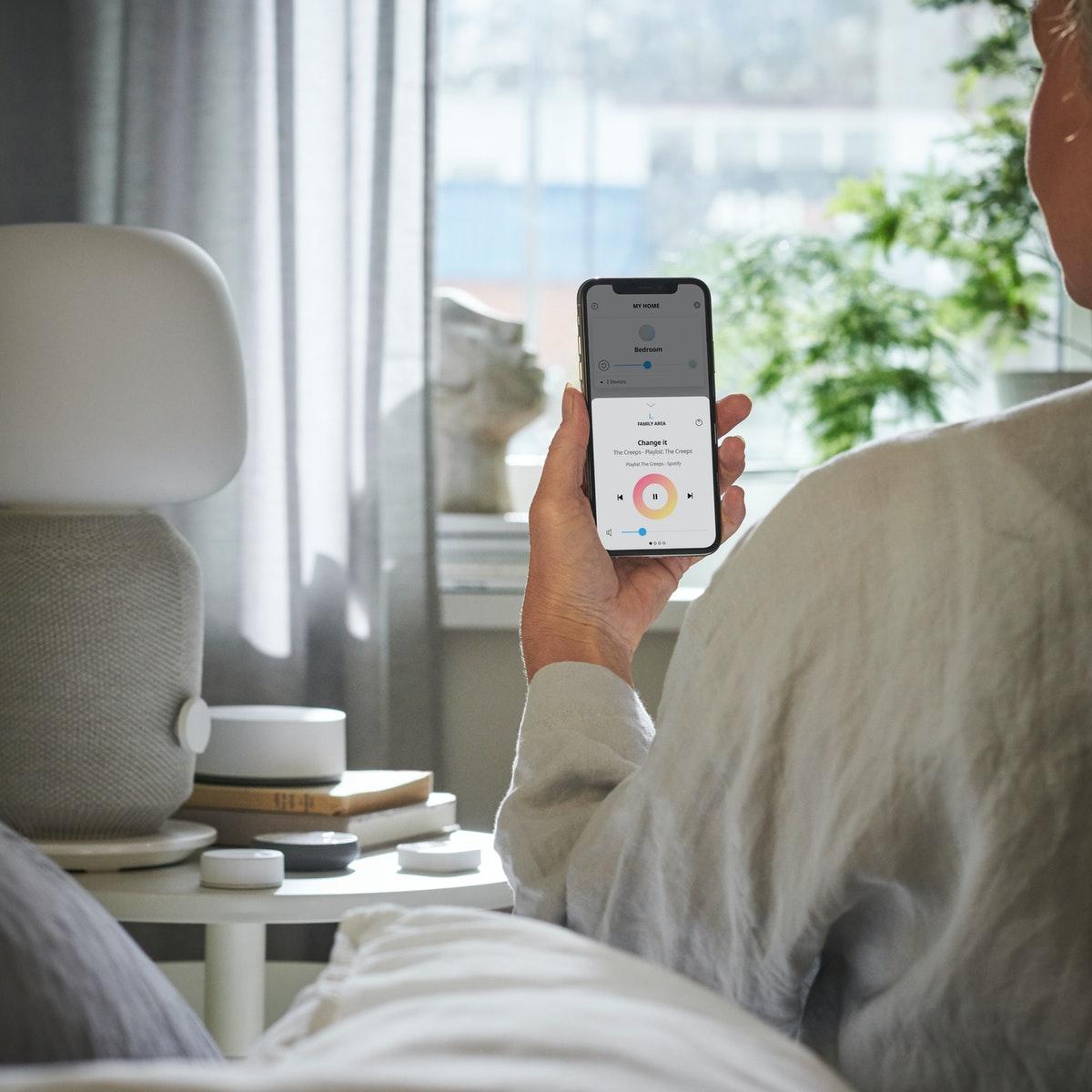 Et menneske sidder på kanten af sin seng og tænder for lyset med sin smartphone