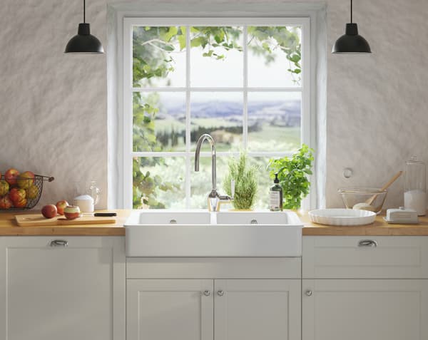 Et nærbillede af en håndvask med ting og sager omkring på køkkenbord foran et vindue med udsigt over et landskab.