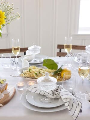 Et opdækket bord med hvid dug, fyldte champagneglas og fad med citronpasta.