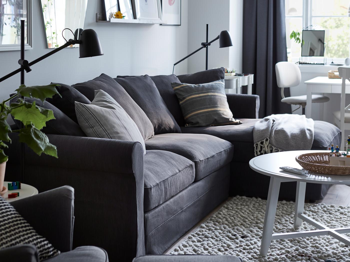 Et rum med en GRÖNLID sovesofa med chaiselong, to SKURUP gulv-/læselamper i sort og diverse malerier på væggen.