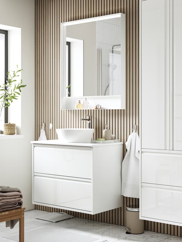 Et solbeskinnet badeværelse i moderne stil med træpaneler på væggen og hvide badeværelsesmøbler.
