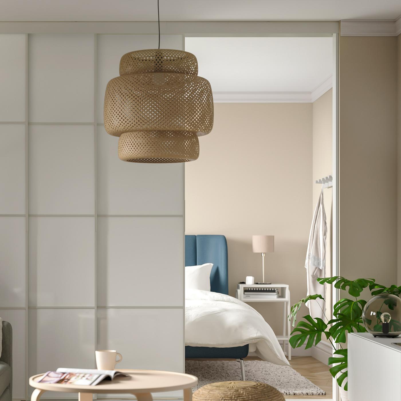 Et soveværelse med en blå seng gemmer sig bag hvide gulv-til-loft-skydedøre. Foran hænger en loftlampe i bambus.