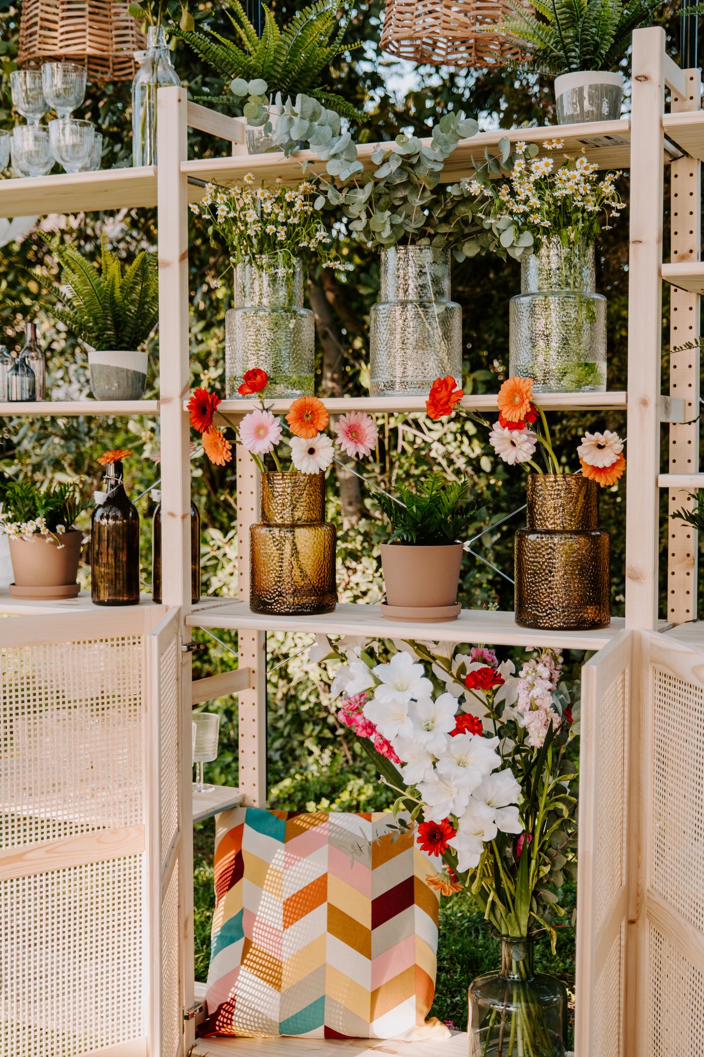 Etagère en bois dehors remplie de vases et de fleurs colorées.