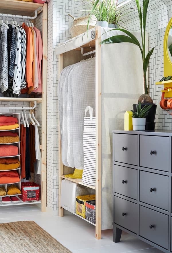 Etagère IKEA IVAR avec tablettes, rails et housse en toile écrue à côté d'une commode BRYGGJA grise dans une chambre
