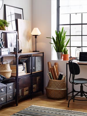 Etagères et bureau en bois et métal noir donnant un style industriel accompagnés d'accessoires comme des tableaux, boîtes de rangement, plantes etc.