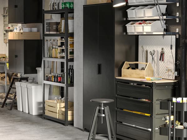 Étagères noires ouvertes et fermées BROR alignées le long du mur d’un garage. Poubelles de tri HÅLLBÄR et boîtes KNAGGLIG sur le sol.