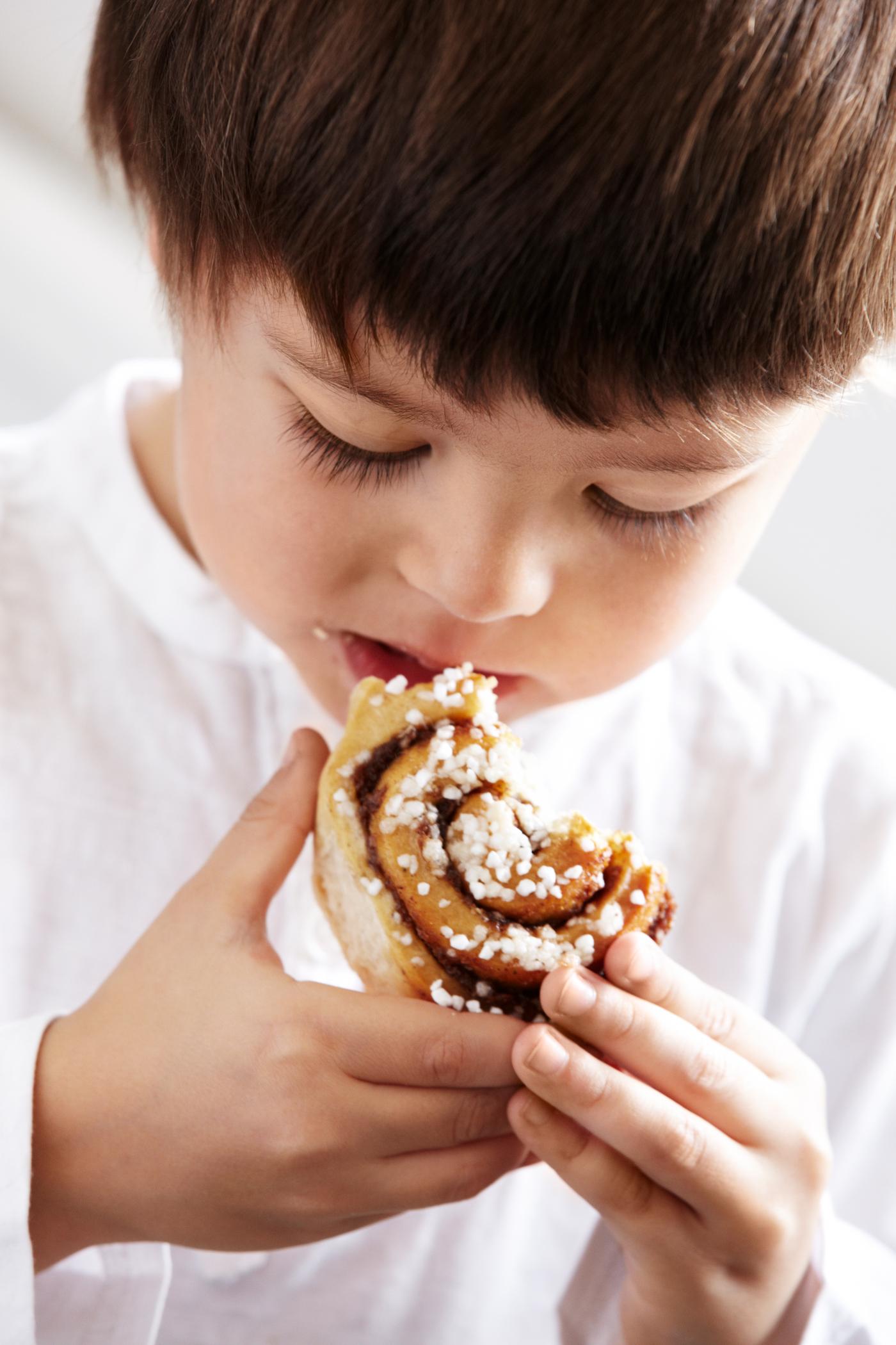 Ett barn i vit tröja tar ett bett av en kanelbulle.