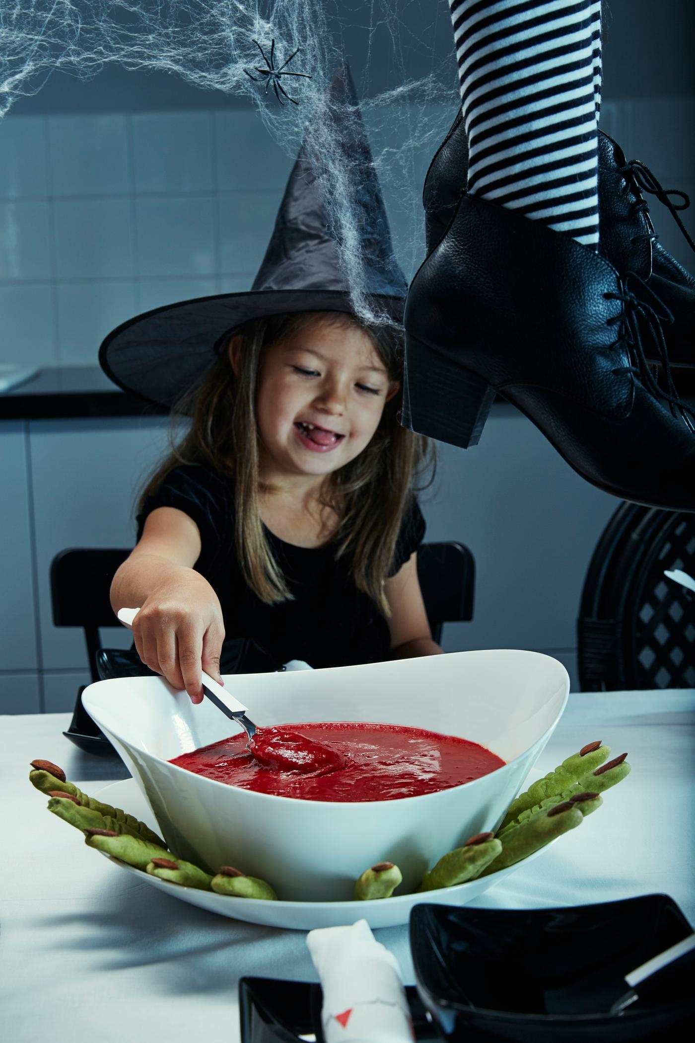 Ett barn med en häxhatt som sitter med en skål med tomatsoppa som ser ut som blod.