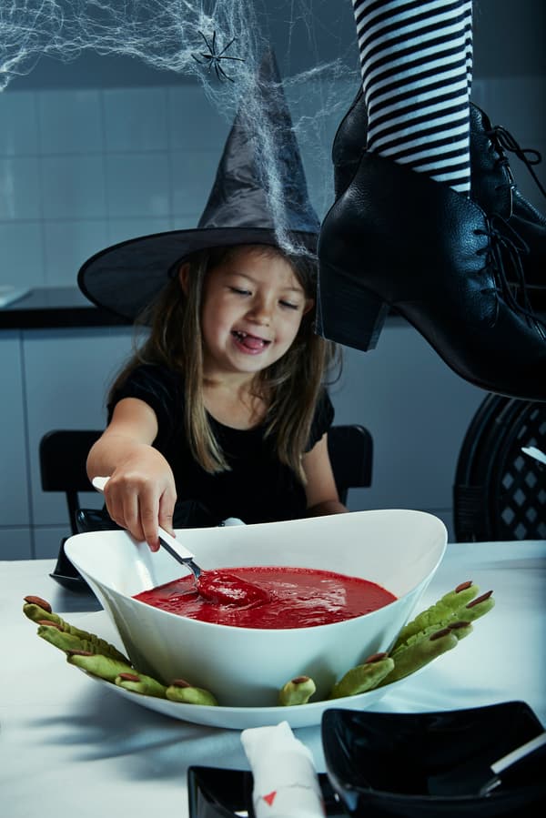 Ett barn med en häxhatt som sitter med en skål med tomatsoppa som ser ut som blod.