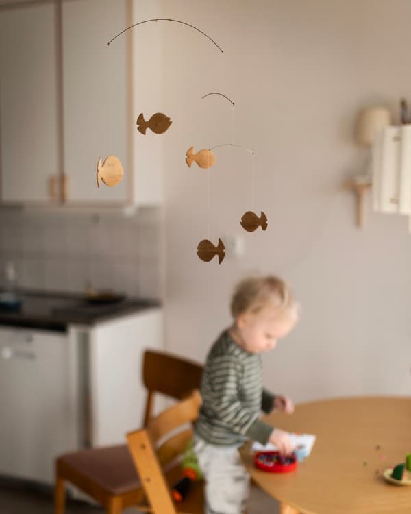 Ett barn står på en tripptrapp-stol vid ett bord. Framför barnet på bordet står leksaker. 