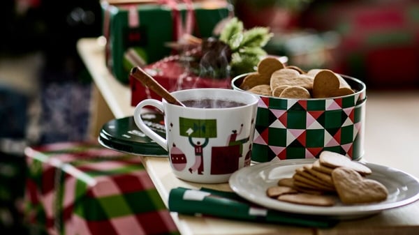 Ett bord med en julkopp med varm dryck, pepparkakor och juldekorationer i bakgrunden.