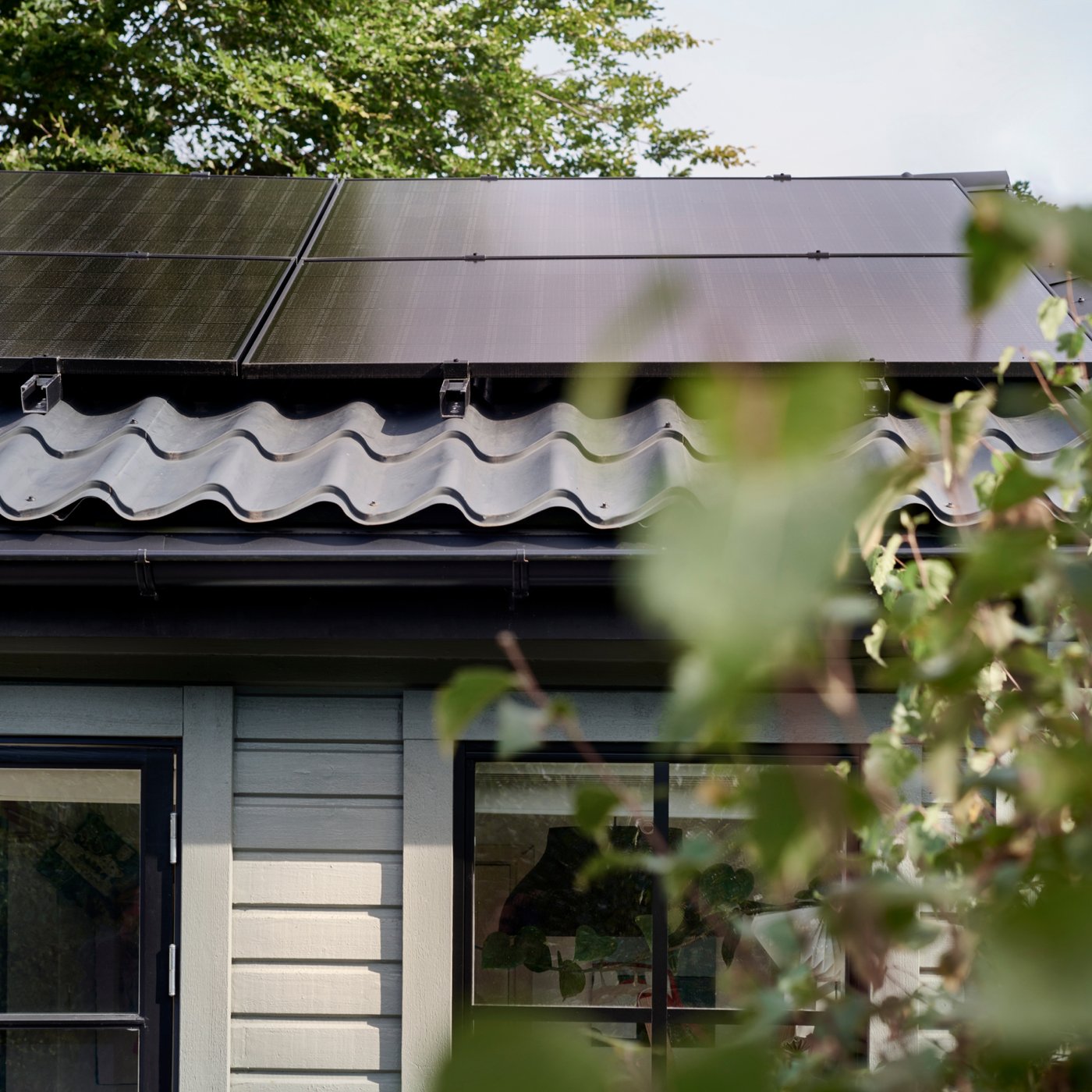 Ett hus med ljus panel-fasad med svart tak och solceller på taket.