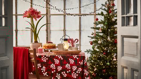 Ett juldekorerat rum med en klädd julgran, en bordduk med julmotiv och en blommande amaryllis på bordet.