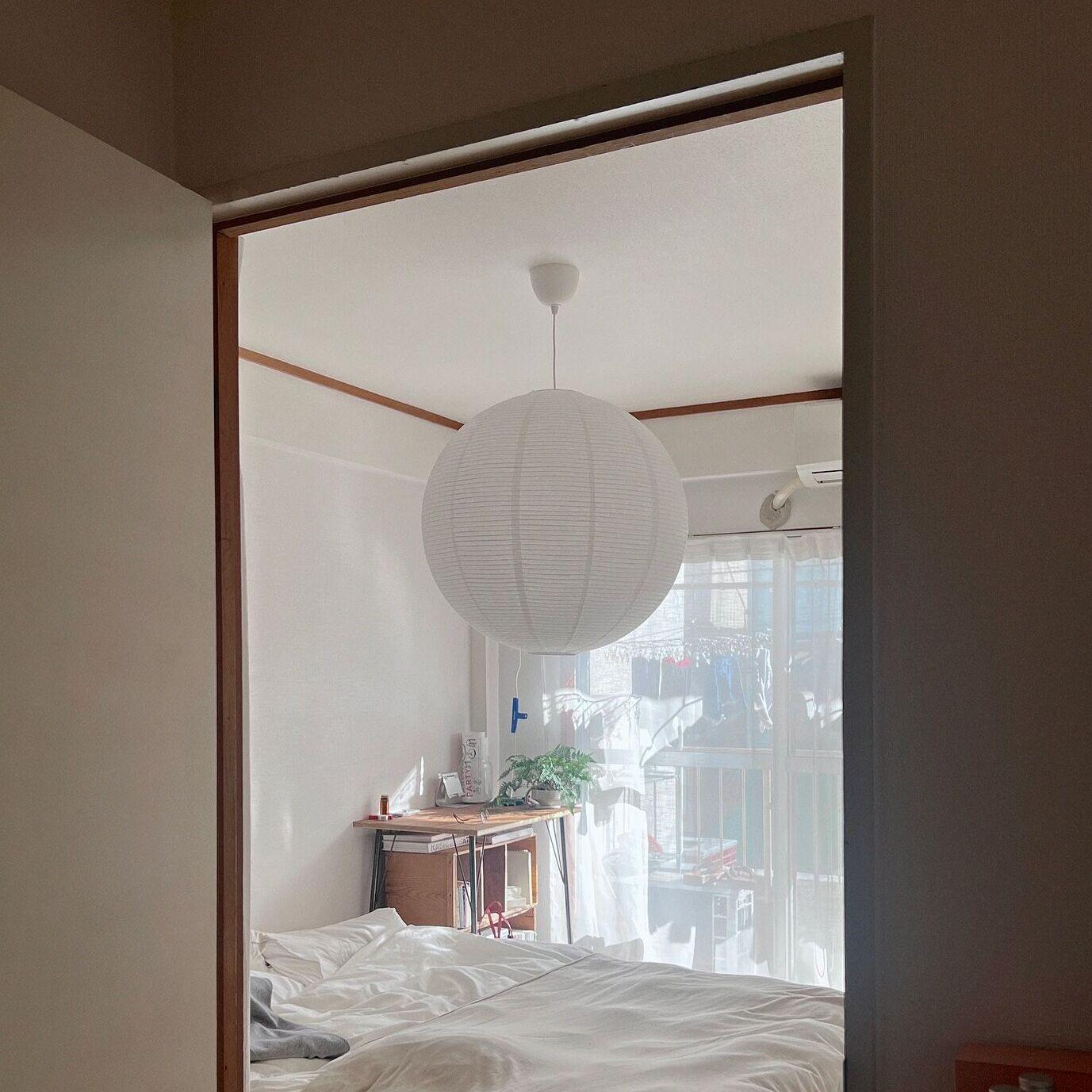 Ett ljust sovrum med en stor vit GULLSUDARE taklampa över en obäddad säng, sett genom en dörröppning, med skrivbord och fönster i bakgrunden.