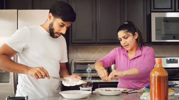 Ett ungt par som ler och förbereder en måltid tillsammans under koncentration.