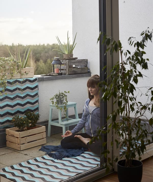Eva practises yoga on a mat on the balcony with plants.