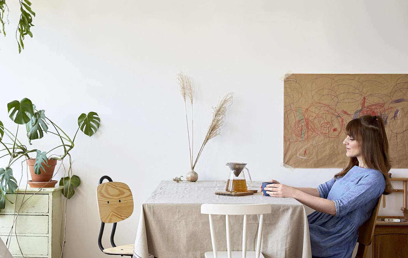 Eva seduta al tavolo della cucina davanti a una tazza di tè e una teiera in vetro - IKEA