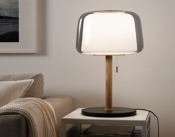 EVEDAL table lamp lit up on a coffee table beside a sofa in the living room, to illustrate IKEA home design service