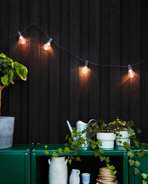 Evening light and a wall where a lit SVARTRÅ LED lighting chain is mounted. The light bulbs give a warm glowing light.
