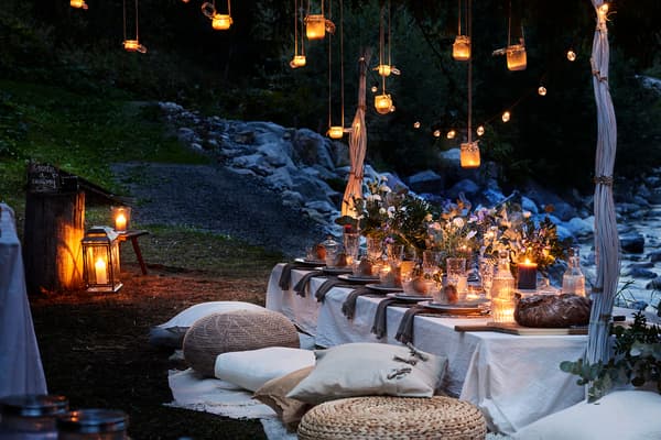 Evening outdoor setting with a boho styled table with cushions around the table and lit lanterns and fairy lights.