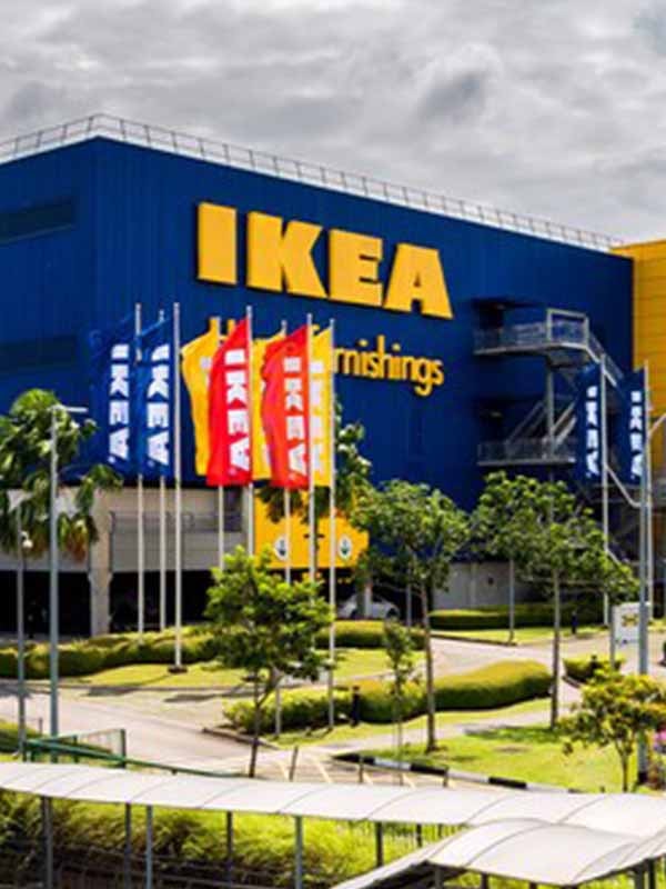 Exterior of IKEA Tampines, with "IKEA" logo on the blue walls. There are red, blue and yellow flags with white "IKEA" logo raised in front of the building.