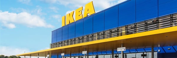 Exterior view of an IKEA store with the large yellow IKEA sign on a blue building, set against a partly cloudy sky.
