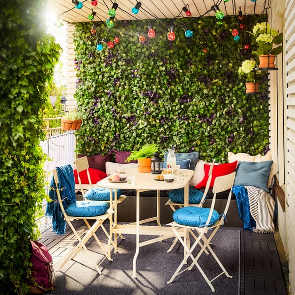 A balcony with a fully extended SALTHOLMEN gateleg table and four chairs in beige. Bright coloured cushions and string lights add a vibrant touch.