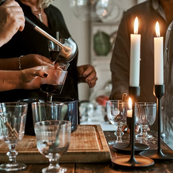 Pessoas de pé junto a uma ilha de cozinha com copos e velas acesas, e uma panela com ponche quente. Uma das pessoas está a verter a bebida num copo.