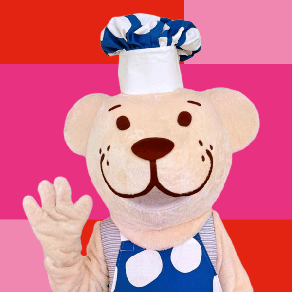 Fabler er klædt ud i sit fineste kokketøj og står foran en pink og rød baggrund og vinker.