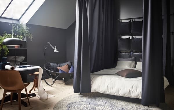 Facile de créer un espace sommeil très douillet à l’aide de quelques articles IKEA. D’abord, fixer au plafond des tringles qui délimiteront la zone autour du lit. Montré ici, le lit KOPPARDAL en acier peint gris. Ensuite, suspendre des rideaux, comme les SANELA en velours de coton bleu foncé.