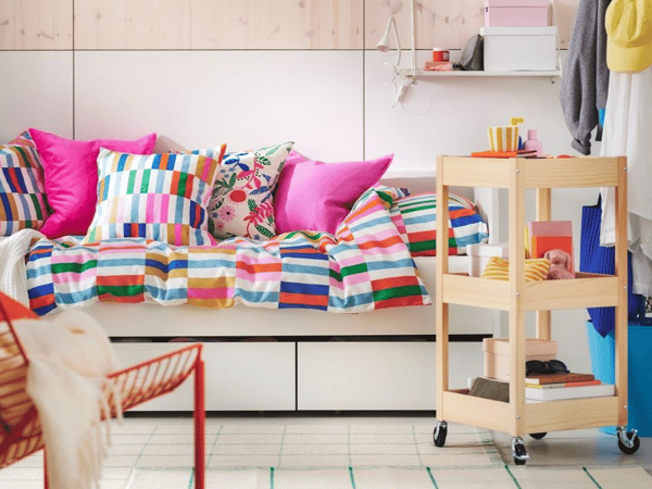 Färgglad säng med en rullvagn i trä bredvid.