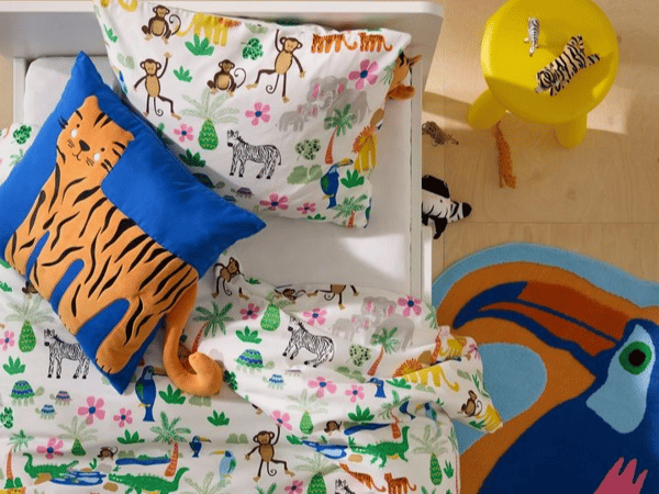 Färgglada sängkläder ses ivanifrån. Kudden är blå med en katt på.