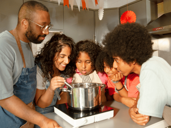 Família de cinco a mexer o conteúdo de uma panela IKEA 365+ numa placa de indução portátil TILLREDA.