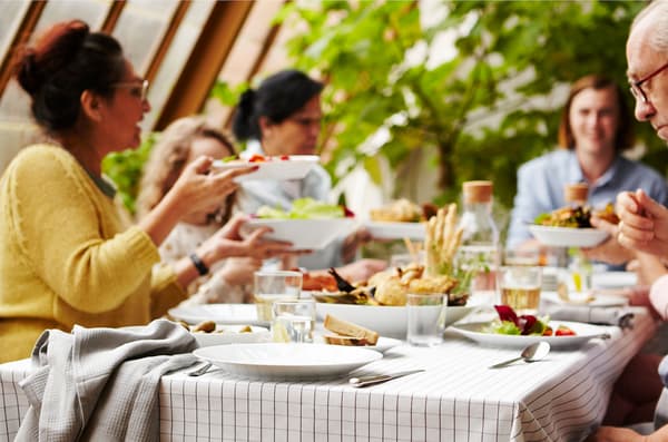 Familia e amigos ao redor dunha mesa con xogos de pratos e cubertos brancos IKEA 365+.