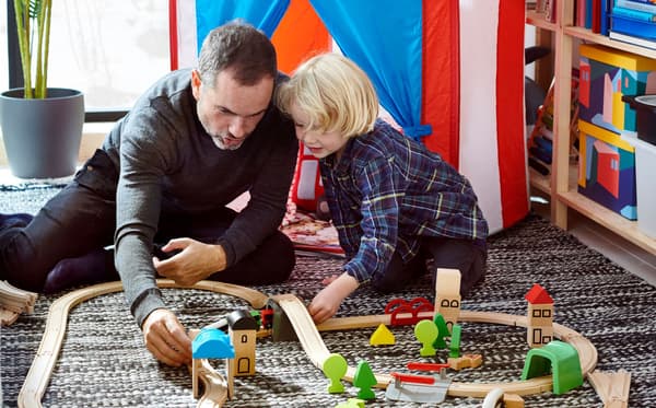 Father and child playing with LILLABO toy train set at home, with a striped play tent in the background.