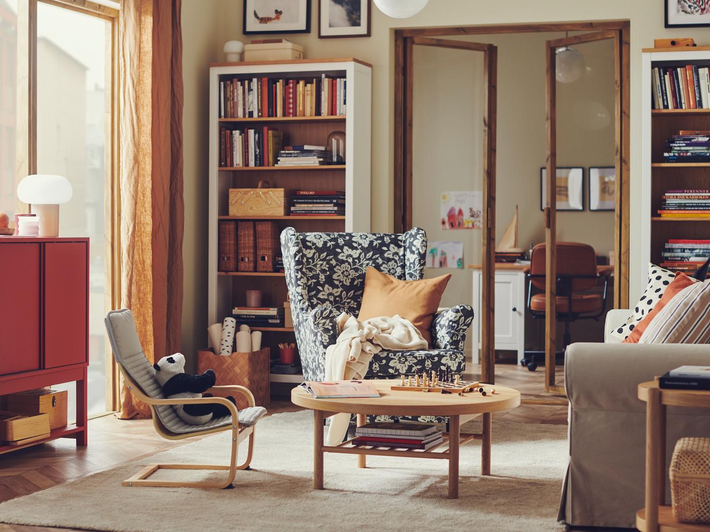Fauteuil à oreilles STRANDMON dans un salon chaleureux et traditionnel avec une bibliothèque HEMNES remplie de livres et d’objets.