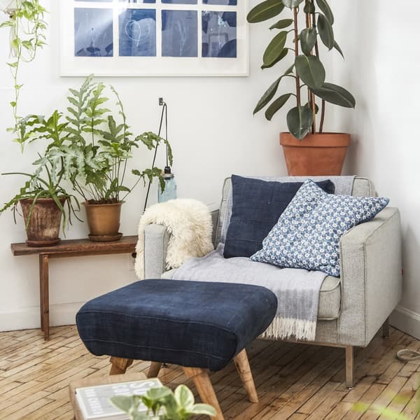 fauteuil avec coussins et plaid , repose pied devant et entouré de plantes vertes