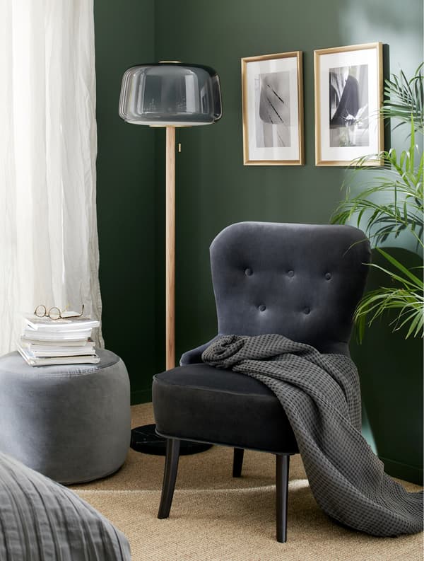 Fauteuil en velours gris, lampadaire gris, pouf gris foncé, plaid gris et cadres dorés.