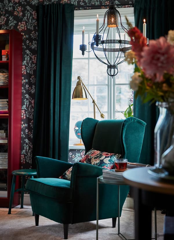 Fauteuil IKEA STRANDMON en velours vert foncé près d’une fenêtre et rideaux SANELA en velours vert foncé.